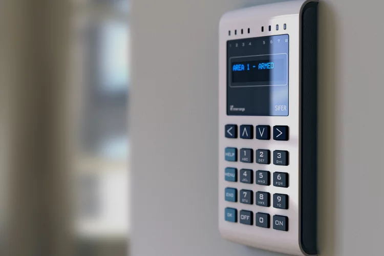 Silver wall-mounted security keypad with a blue digital display reading "AREA 1 - ARMED".