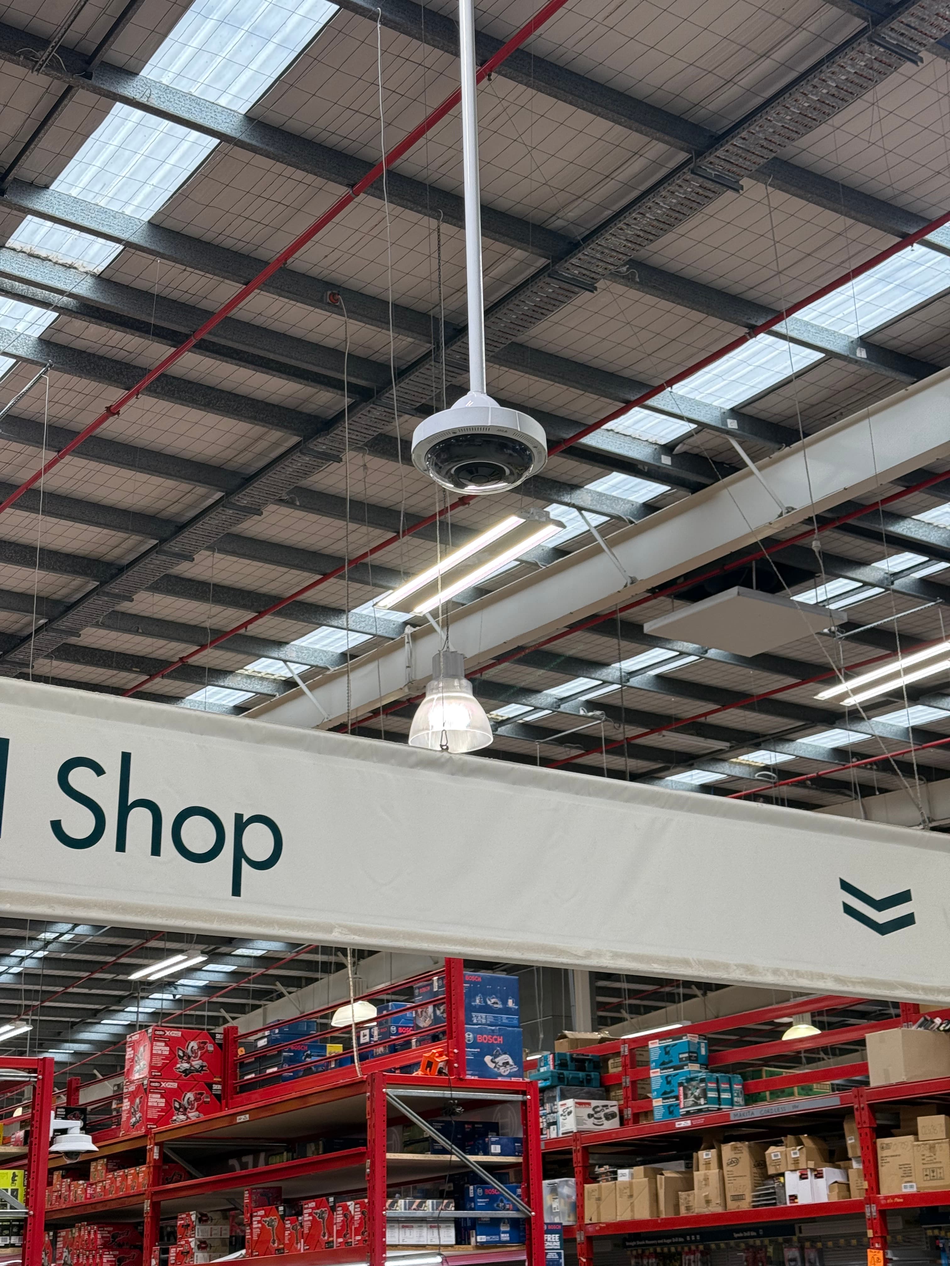 Warehouse interior featuring a security camera, hanging Shop sign, and high ceilings with skylights.