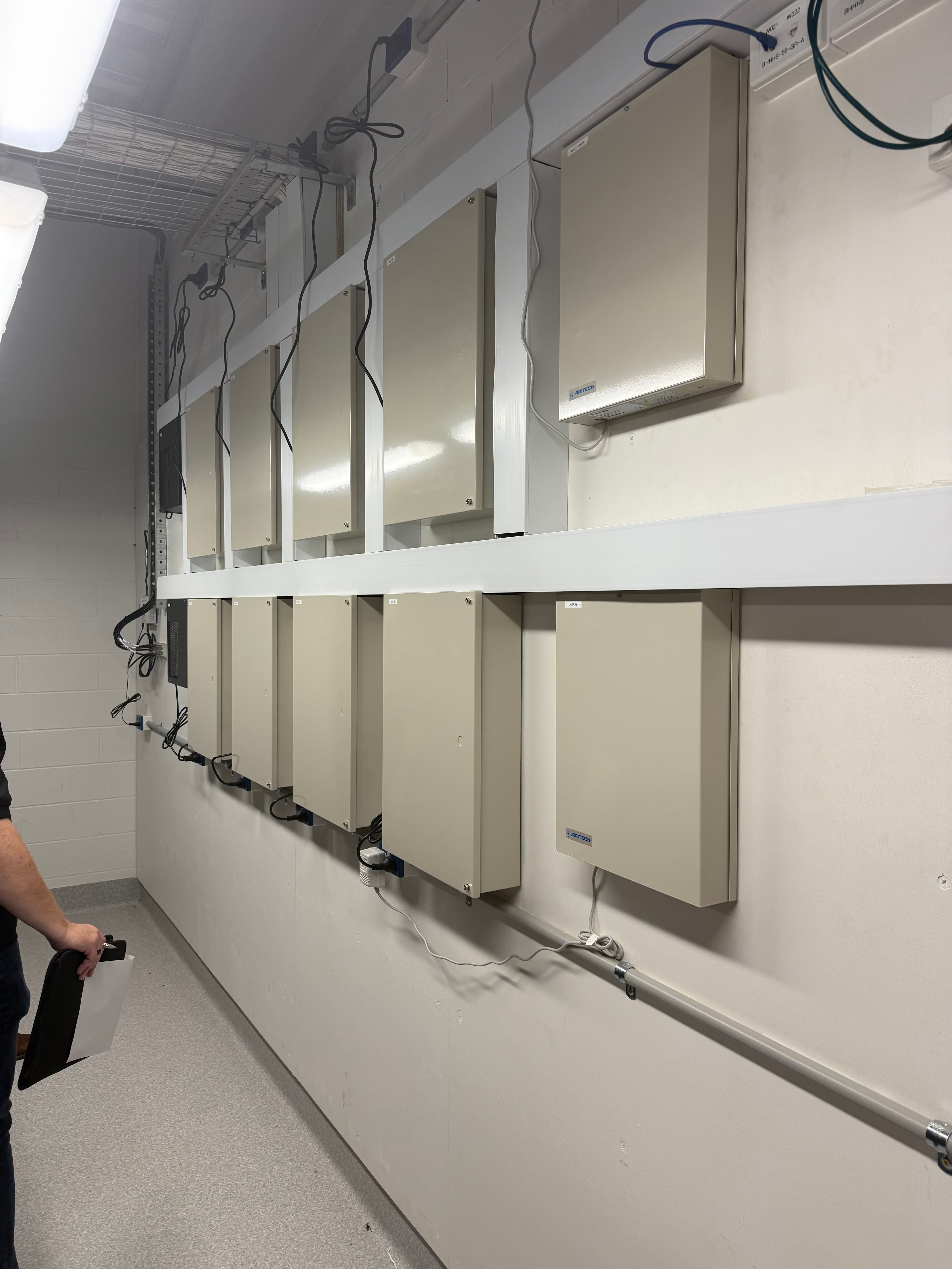 Beige Aritech control panels mounted in rows on a white ceiling with connected wiring.
