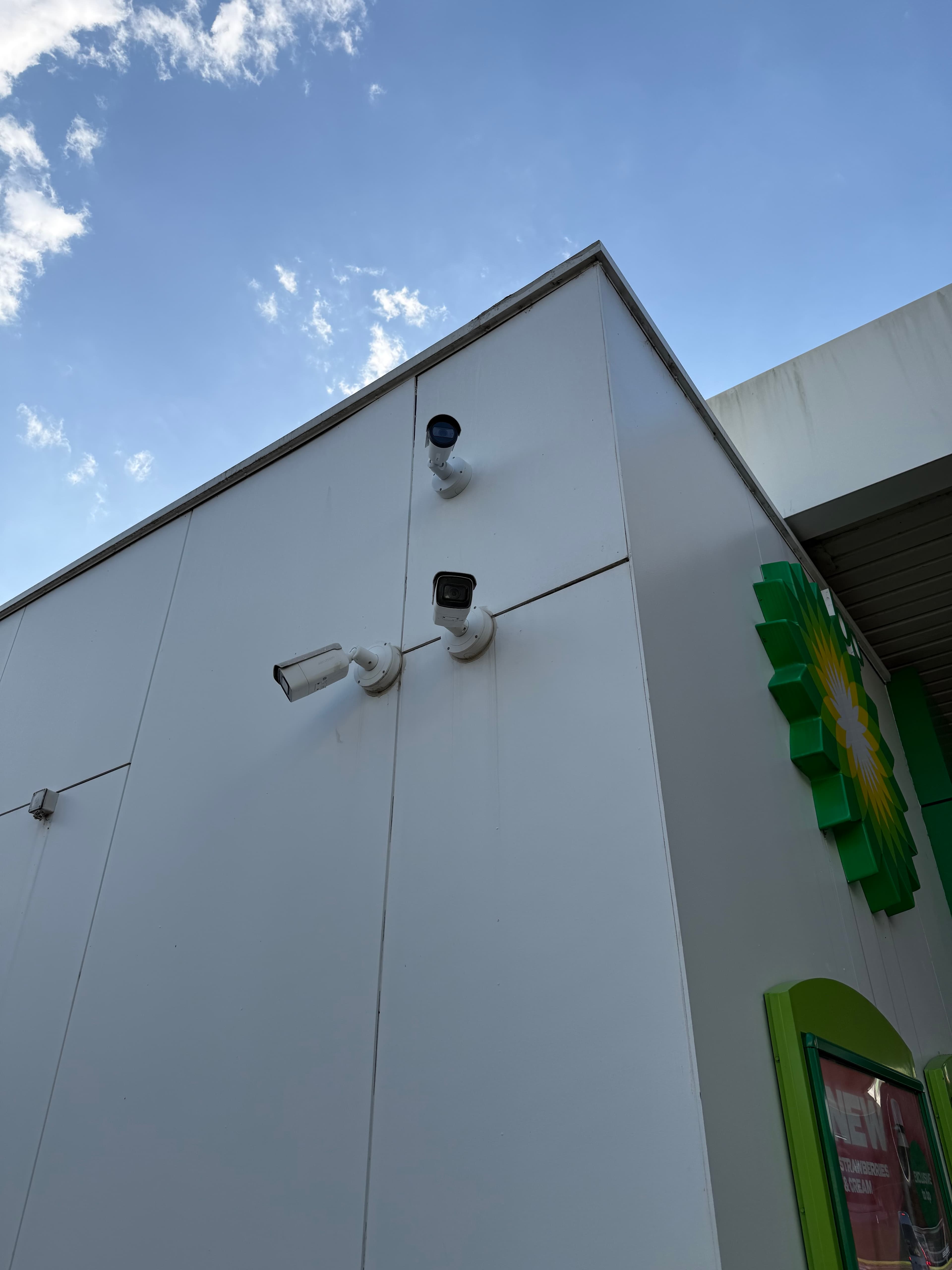 Three white security cameras mounted on a white building wall under a bright blue sky.