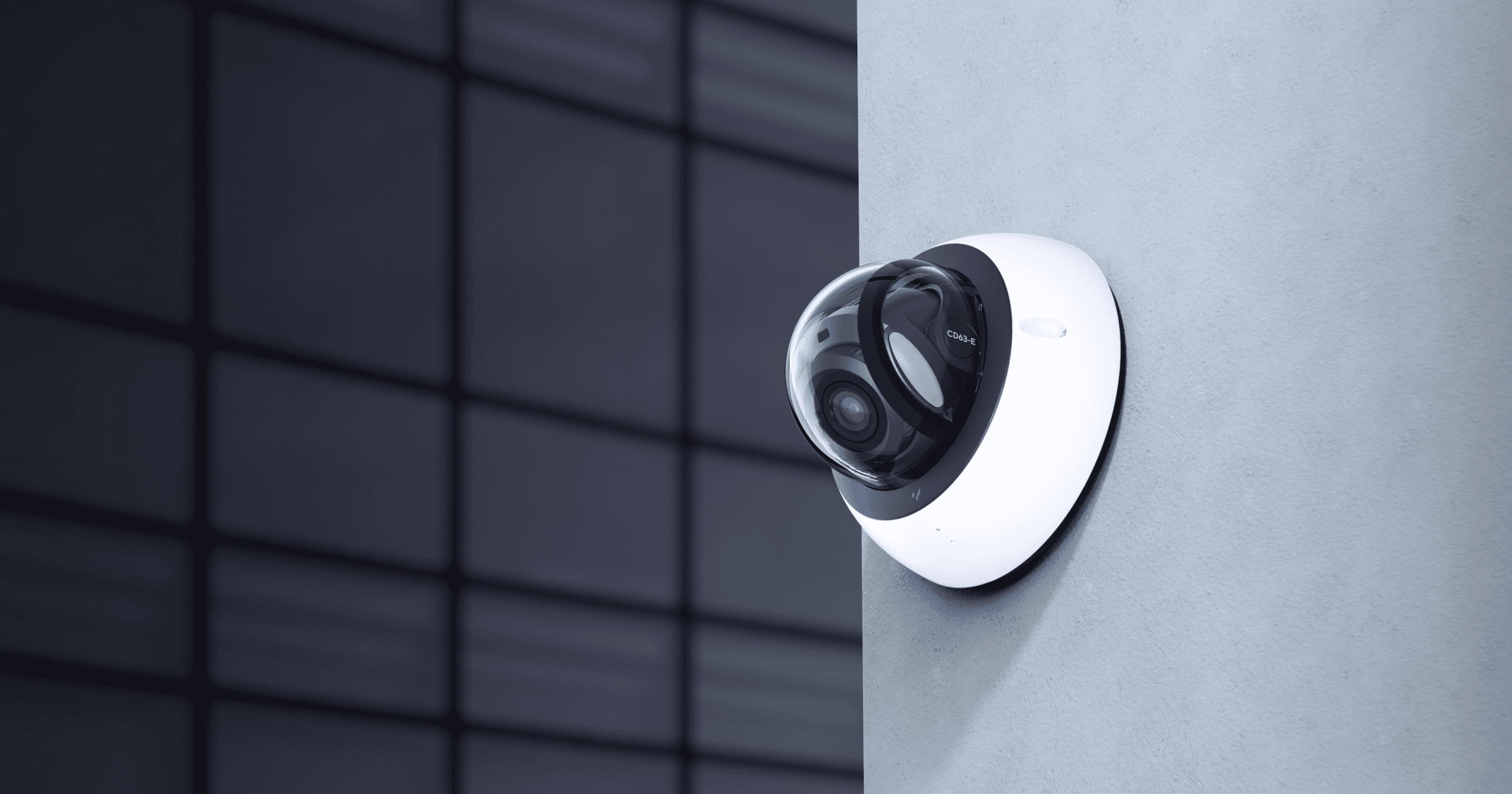 Sleek white dome security camera mounted on a wall with a dark glass building background.